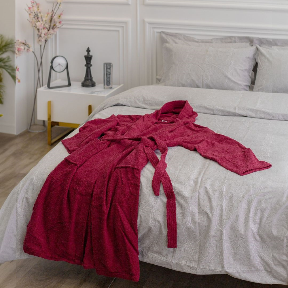 Red bathrobe lying on grey paisley-pattrened bedding